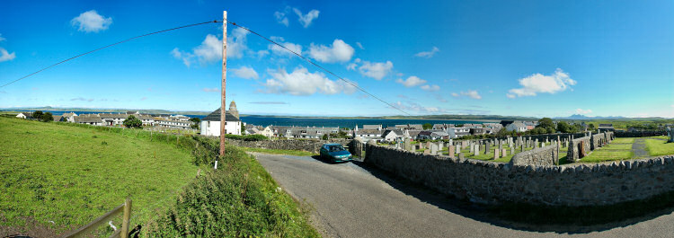 Picture of a panoramic view of a coastal village (Bowmore on the Isle of Islay) with a round church in the foreground. A large sea loch (Loch Indaal) in the background