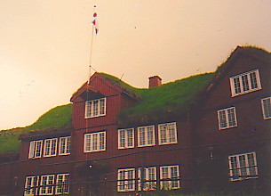 Picture of the Faroese parliament, a wooden building with a grass roof, flag pole on outside