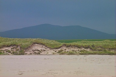Picture of dunes in the sun with a hill under dark clouds behind it