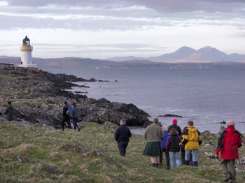 Walkers approaching Port Charlotte lighthouse, the Paps of Jura in the background