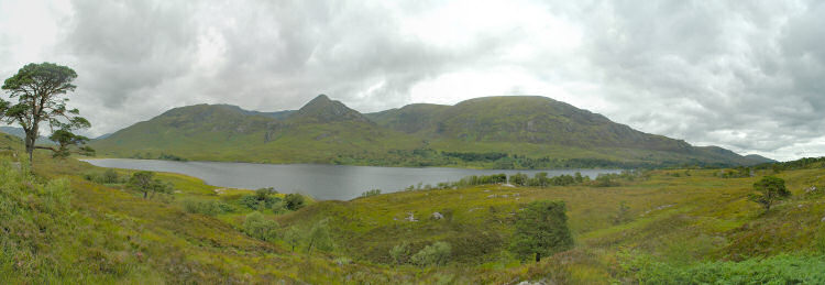 Picture of a panoramic view over a glen and a loch, mountains behind the loch