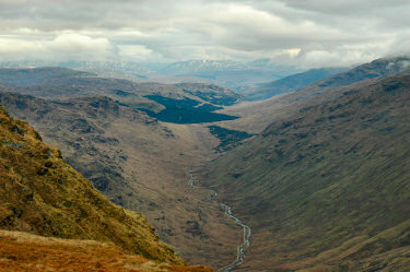 Picture of a view along a glen, snow covered mountains in the distance