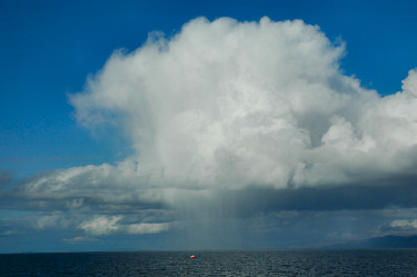 Picture of a huge rain cloud with rain falling on a tiny boat