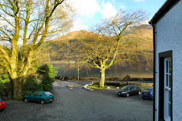 Picture of a view out of a window over a car park, a loch and some hills