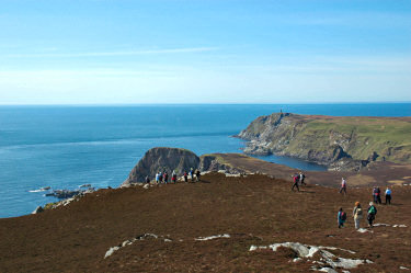 Picture of walkers decending from a hill towards some cliffs