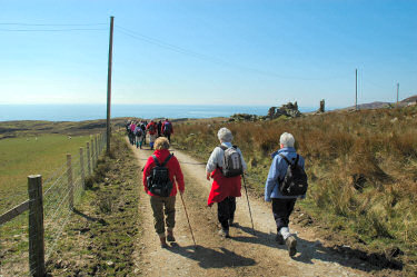 Picture of a group of walkers approaching some ruins, the sea in the background