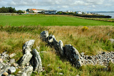 Picture of the remains of a neolithic cairn with a village (Port Charlotte, Islay) in the background