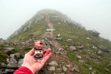 Picture of a hand holding a compass with a path going into clouds behind it
