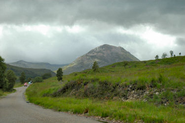 Picture of mountain with some sunshine brightening it up, single track road in the foreground