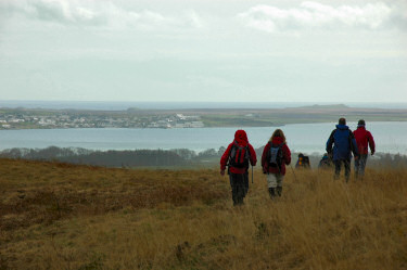 Picture of walks walking over the top of a hill, a sea loch with a village on the other side coming into view