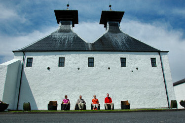 Picture of a family sitting in chairs made from casks in front of a distillery