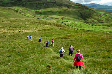 Picture of a group of walkers descending a hillside towards the ruins of an old building