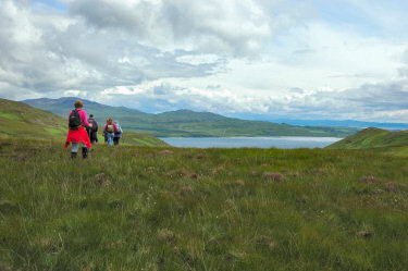 Picture of walkers going over a crest with a sound between two islands coming into view