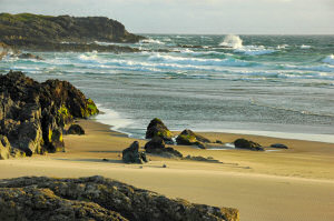 Picture of a beach and rocky shore with breaking waves in the evening sun