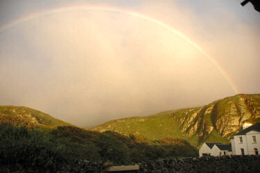Picture of a developing rainbow above a house in front of crags