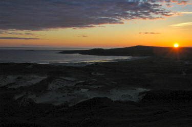 Picture of the sun setting over some low hills near a shore, almost gone at this stage