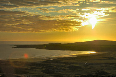 Picture of the sun setting over some low hills near a shore