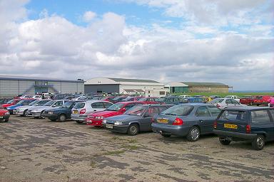 Cars parked on the runway with the hangars in the background