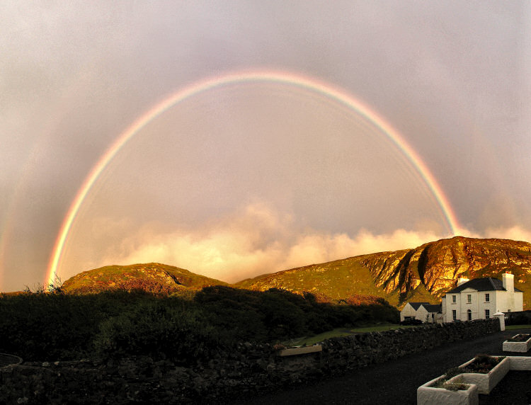 Picture of a full rainbow above crags and a house
