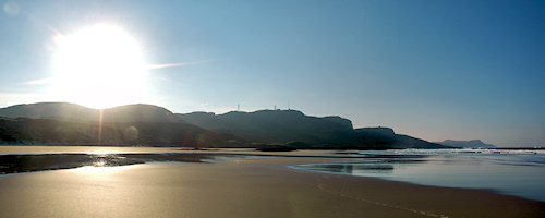 Picture of the sun rising above some crags towering above a golden sandy beach