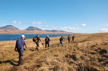 Picture of walkers walking along a sound between two islands, high hills on the other side of the sound